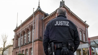 Vor dem Landgericht Verden steht ein Mann mit "Justiz"-Jacke.