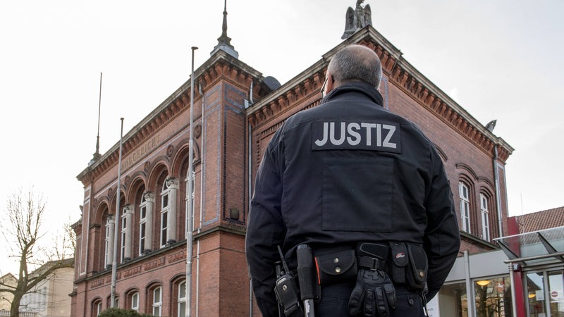 Vor dem Landgericht Verden steht ein Mann mit "Justiz"-Jacke.