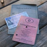 Drei verschiedene Führerschein-Generationen auf einem Bild. Der alte Graue, der neuere in Rosa und die aktuell übliche Plastikkarte.