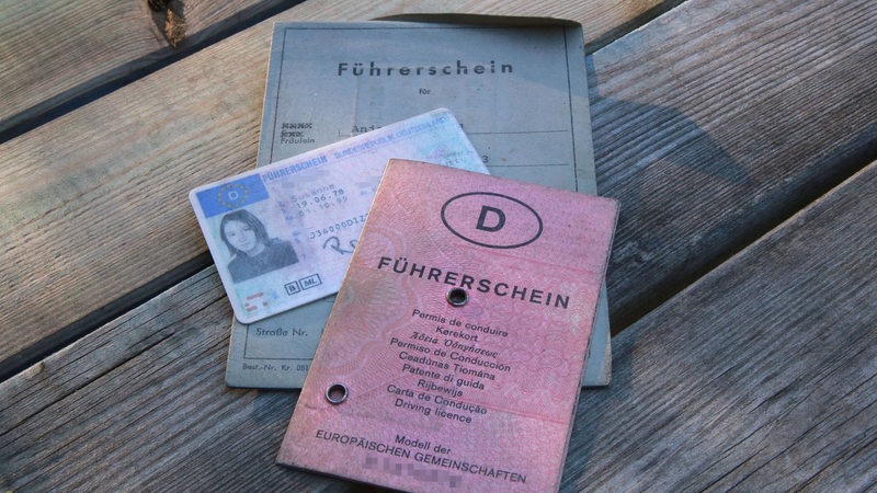 Drei verschiedene Führerschein-Generationen auf einem Bild. Der alte Graue, der neuere in Rosa und die aktuell übliche Plastikkarte.