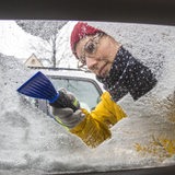 Junge Frau befreit ein Auto von Eis und Schnee.