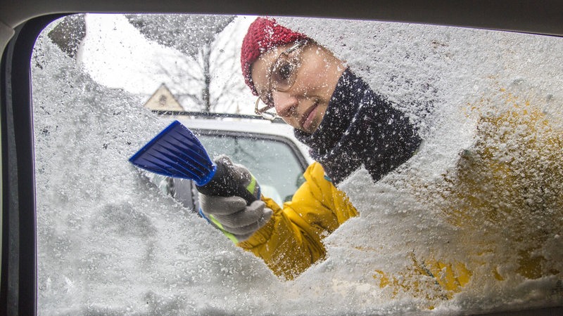 Junge Frau befreit ein Auto von Eis und Schnee.