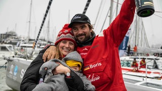 Weltumsegler Boris Herrmann glücklich nach der Ankunft mit Frau und Tochter im Arm.