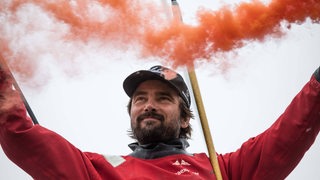 Boris Herrmann hält bei seiner Zieleinfahrt zwei gezündete Bengalos in die Höhe.