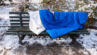 Ein blauer Schlafsack liegt auf einer Bank im Schnee.