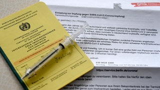 Ein Impfpass mit einer Spritze auf einem beschriebenen Zettel.