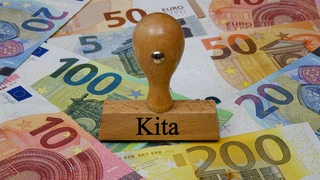 Auf Geldscheinen liegt ein Stempel mit der Aufschrift "Kita"