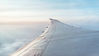Ein Flugzeugflügel mit Wolken im Hintergrund.
