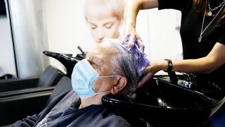 Eine Seniorin bekommt von einer Friseurin die Haare gewaschen und trägt dabei einen Mund-Nasenschutz.