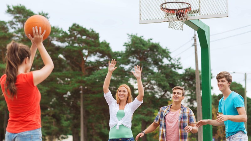 Vier junge Menschen spielen auf einem Freiplatz Basketball.