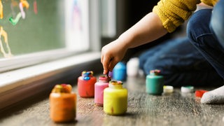 Kinder handtieren mit Farbtöpfen und malen auf eine Scheibe.