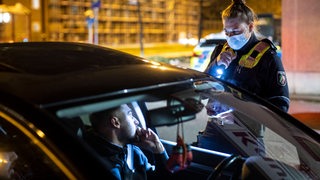 Eine Polizistin mit Taschenlampe kontrolliert einen Autofahrer.