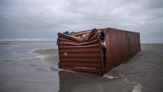 Ein beschädigter Container liegt im Sand.