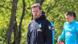 Florian Kohfeldt läuft vor dem Training über das Trainingsgelände. Im Hintergrund folgt ihm Ludwig Augustinsson.