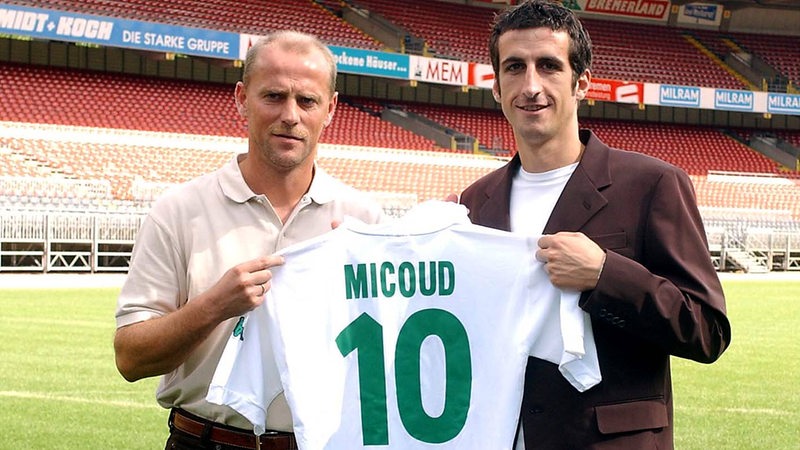Thomas Schaf und Johan Micoud stehen im Weser-Stadion und halten 3in Trikot von Micoud in die Kamera.