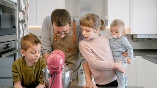 Vater mit drei Kindern an einer Küchenmaschine