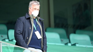 Ein Mann steht mit Maske allein auf einer Tribüne mit Sitzplätzen in einem Fußballstadion