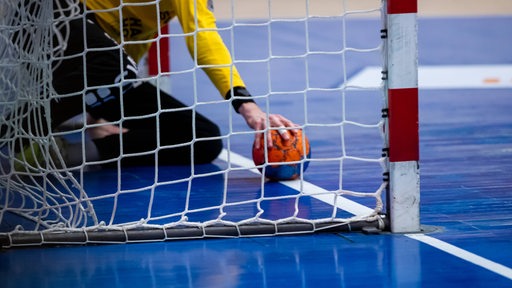 Ein Handball-Torhüter holt einen Ball aus dem Netz.