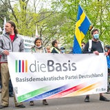 Corona-Demonstranten in Berlin-Lichtenberg halten ein Schild der Partei Die Basis
