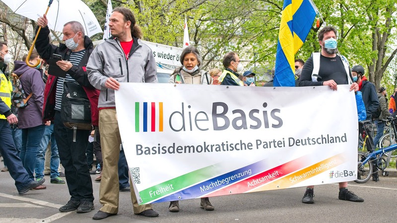 Corona-Demonstranten in Berlin-Lichtenberg halten ein Schild der Partei Die Basis