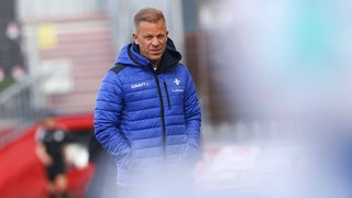 Darmstadt-Trainer Markus Anfang in blauer Jacke mit Händen in der Tasche an der Seitenlinie.