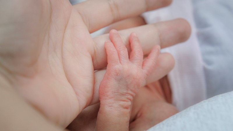 Eine Babyhand greift nach einem Finger