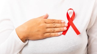 Eine Frau trägt eine rote Aids-Schleife am Pullover (Symbolbild)