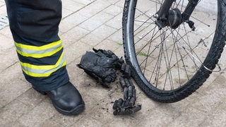 Ein Fahrradakku nach einem Brand, daneben der Fuß eines Feuerwehrmannes (Archivbild)