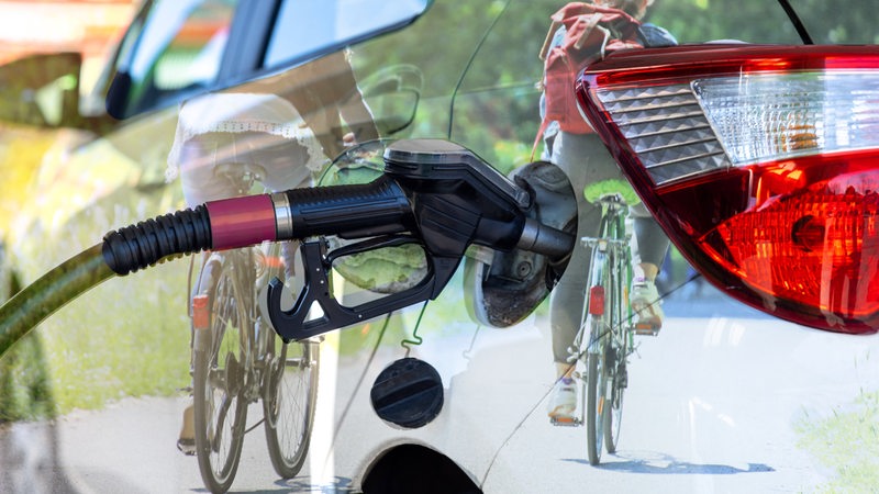 Ein Auto wird betankt, darin spiegeln sich zwei Fahrradfahrerinnen (Montage)