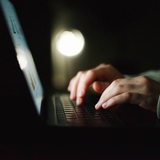 Eine Person schreibt im Dunkeln etwas auf einem Laptop (Symbolbild)