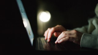 Eine Person schreibt im Dunkeln etwas auf einem Laptop (Symbolbild)