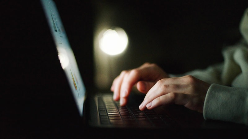 Eine Person schreibt im Dunkeln etwas auf einem Laptop (Symbolbild)