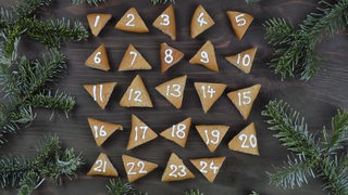 Ein Adventskalender aus Keksen mit Zahlen aus Zuckerguss, drum herum liegen Tannenzweige (Symbolbild)
