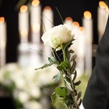 Eine Hand hält eine Rose vor einer geschmückten Urne