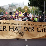 Menschen auf einer Demonstration tragen das Transparent "Die Reichen müssen für die Krise zahlen - wer hat der gibt"
