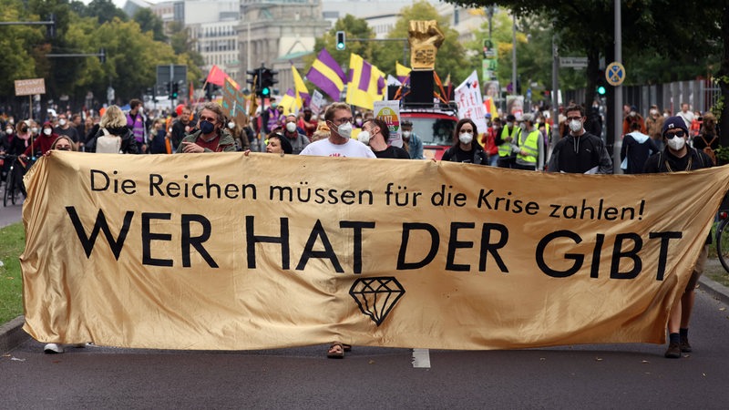 Menschen auf einer Demonstration tragen das Transparent "Die Reichen müssen für die Krise zahlen - wer hat der gibt"
