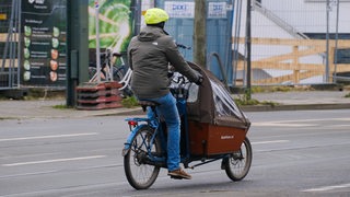 Ein Mann fährt mit einem Lastenrad durch eine Straße.
