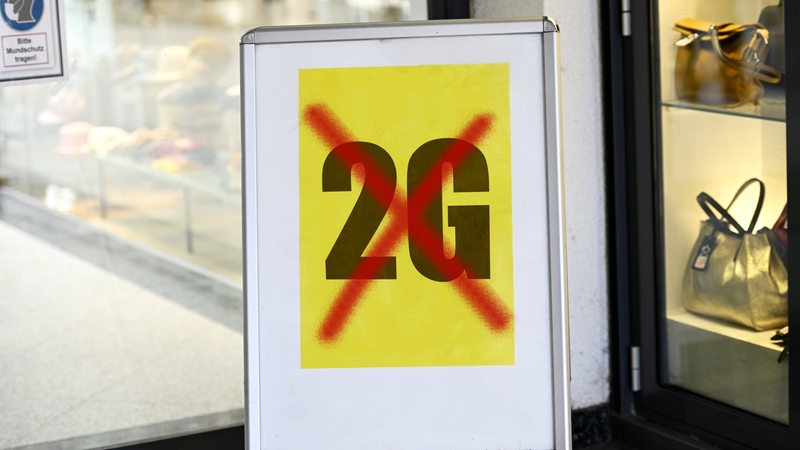 Ein Schild vor einem Laden mit durchgestrichenem 2G Motiv