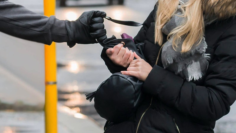 Eine Frau wird an einer Haltestellt von einem Mann angegriffen, der an ihrer Tasche zieht (Symbolbild)