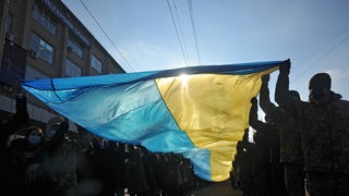 Eine Reihe Menschen hält eine Ukrainische Flagge in die Luft.