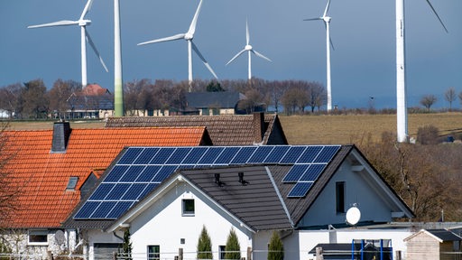 Wohnhäuser mit Solaranlagen im Hintergrund Windkrafträder