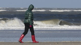 Eine Frau mit roten Gummistiefeln läuft bei Sturm an der Nordseeküste von Langeoog