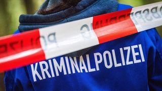 Aufschrift Kriminalpolizei auf einer Jacke hinter Absperrband (Archivbild)