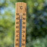 Thermometer aus Holz vor grünen Blättern in der Natur mit der Temperatur 40 Grad Celsius. 