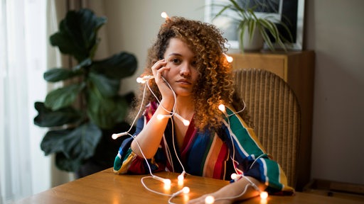 Junge Frau mit Weihnachtsbeleuchtung um den Körper schaut enttäuscht in die Kamera (Symbolbild)