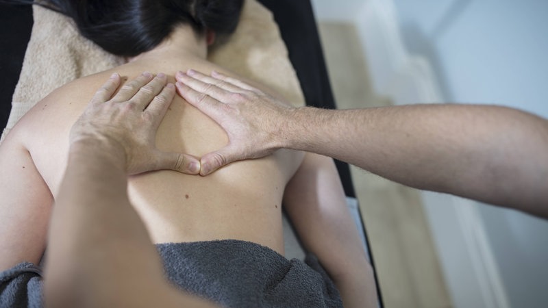 Eine Frau liegt auf einer Massagebank, Männerhände liegen auf ihrem Rücken