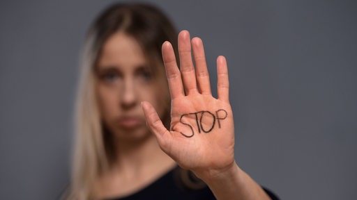 Eine Frau hält ihre Hand hoch, darauf steht das Wort "Stop"