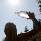 Eine Frau schüttet sich im prallen Sonnenschein zur Erfrischung Wasser aus einer Flasche über den Kopf.