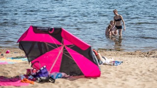 Menschen im Wasser, am Strand liegt ein Sonnenschirm.