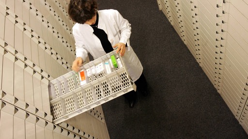 Eine Apothekerin zieht eine nahezu leere Schublade aus einem Medikamentenschrank heraus. (Bildmontage)